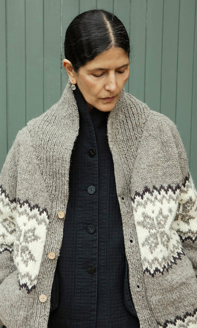 Plümo  A person with dark hair in a bun wears the Shingle Cardigan over a black shirt, looking down.