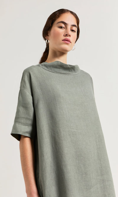 Plümo- Woman in the loose sage green Sims Dress and hoop earrings, posing against a plain background.