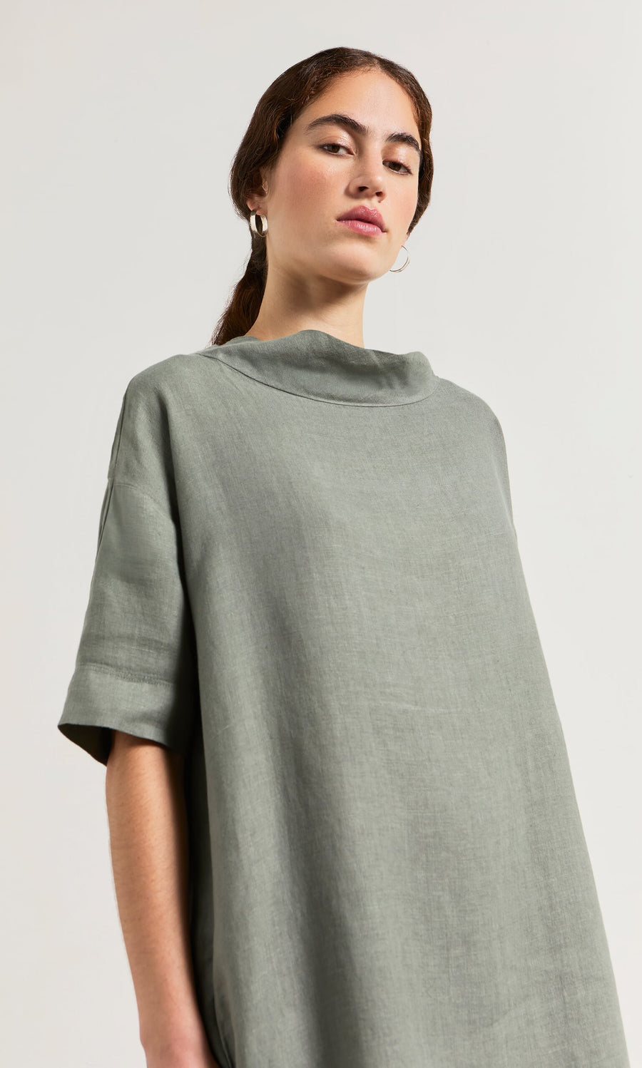Plümo- Woman in the loose sage green Sims Dress and hoop earrings, posing against a plain background.