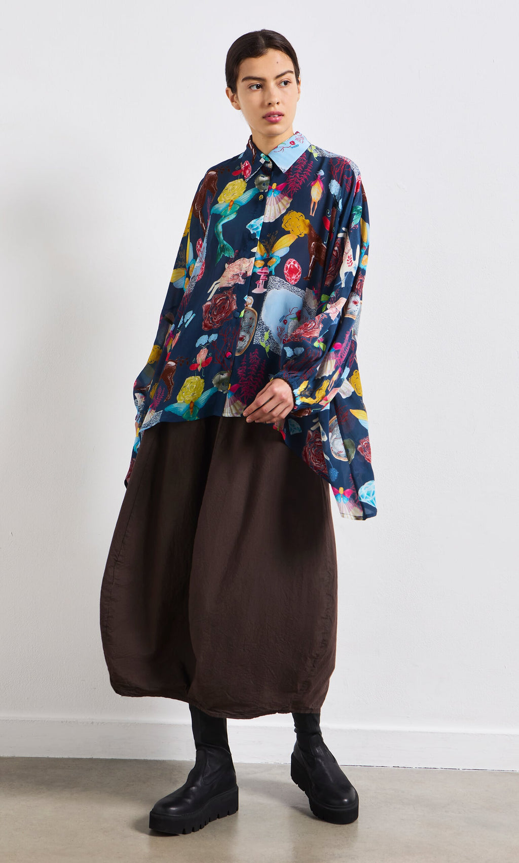Plümo- Person wearing the Sketch Blouse, brown wide-leg pants, and black boots against a white wall.