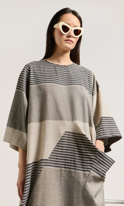 Plümo- Woman in cat-eye sunglasses wears the Stonebar Dress, a loose, striped patchwork monochrome style, against a plain backdrop.