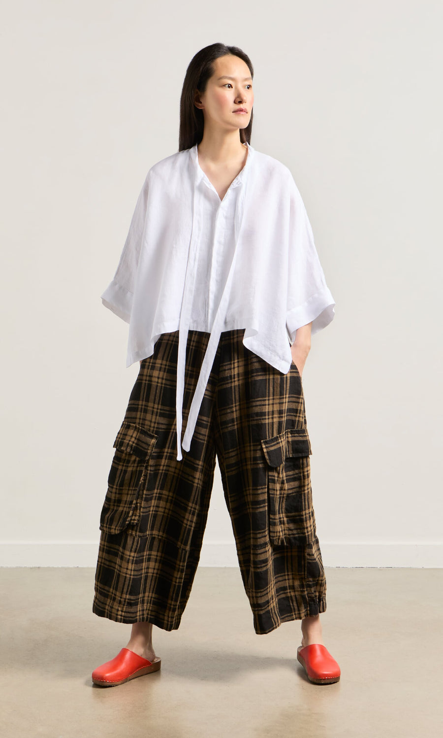 Plümo- Woman in a loose white top and Tam Check Pants with an elastic waist, paired with red slip-on shoes.