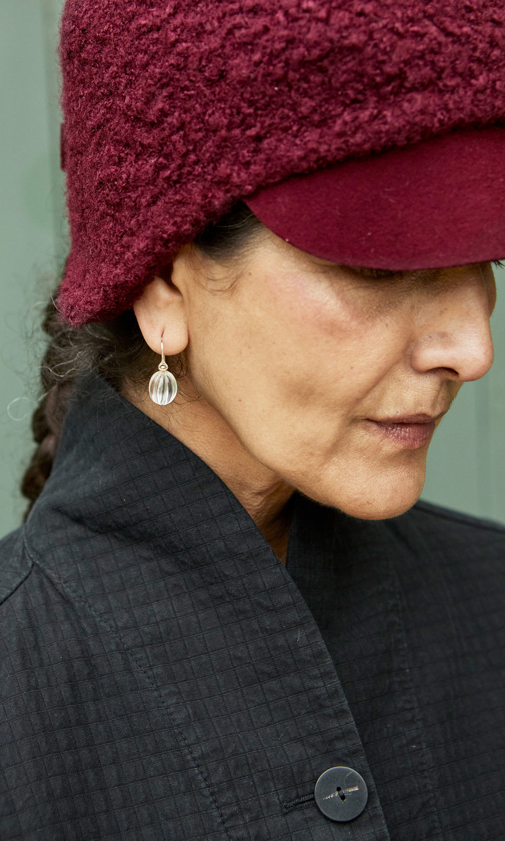 Plümo  Woman in a burgundy textured hat and black coat, facing sideways, wearing handcrafted Tamsin Earrings.