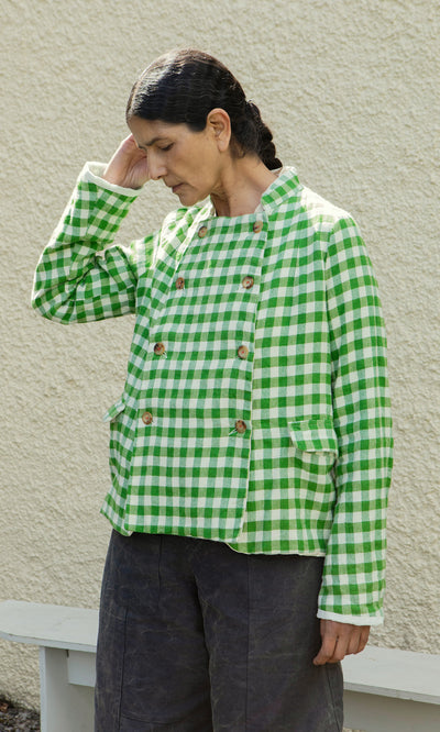 Plümo  Person wearing the Tiree Jacket stands against a textured wall, gazing down thoughtfully.