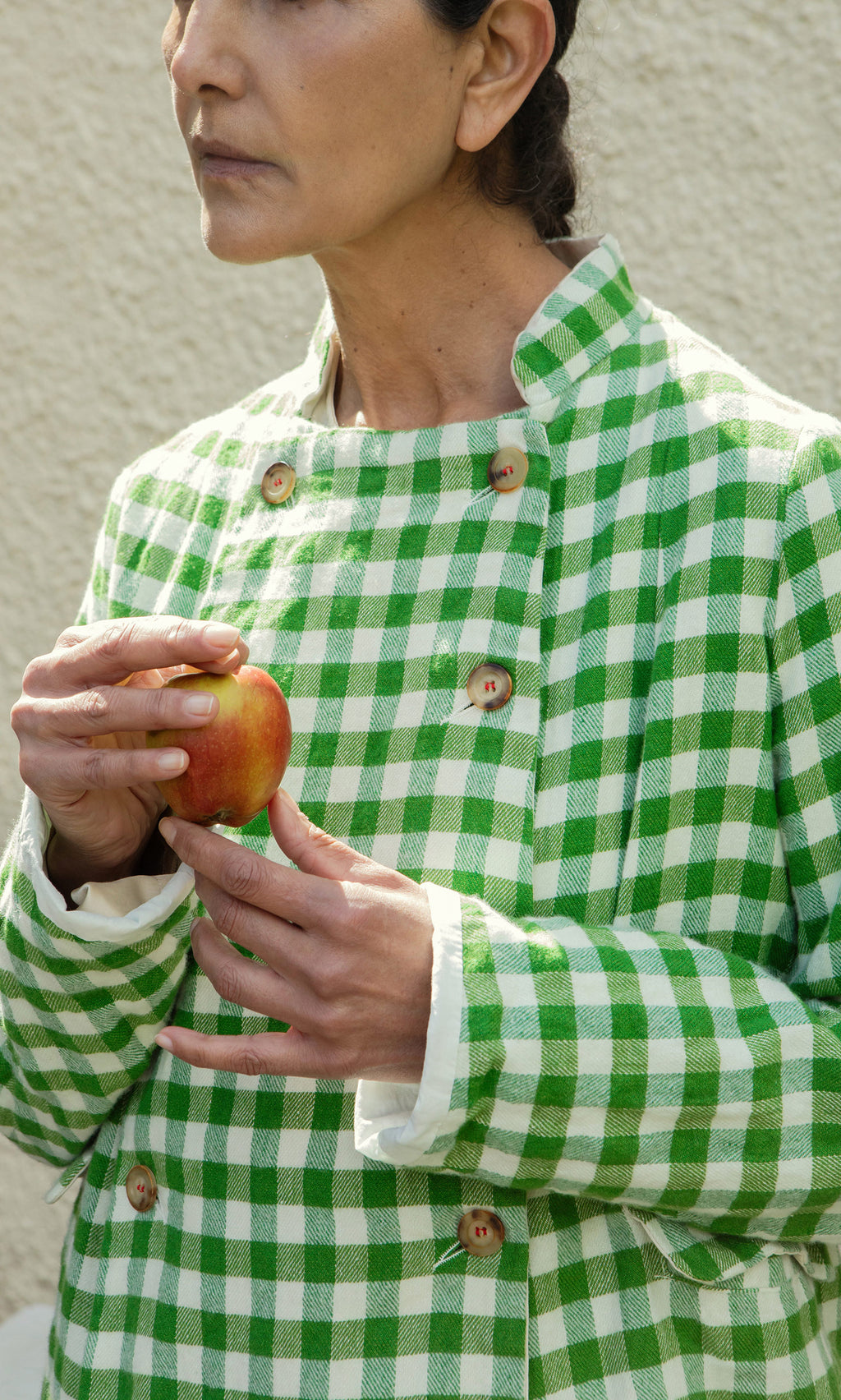 Plümo  Person in a Tiree Jacket holds an apple, standing against a light textured wall.