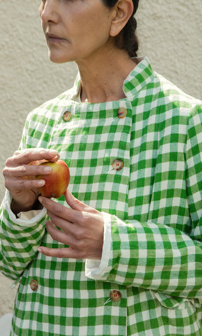 Plümo  Person in a Tiree Jacket holds an apple, standing against a light textured wall.