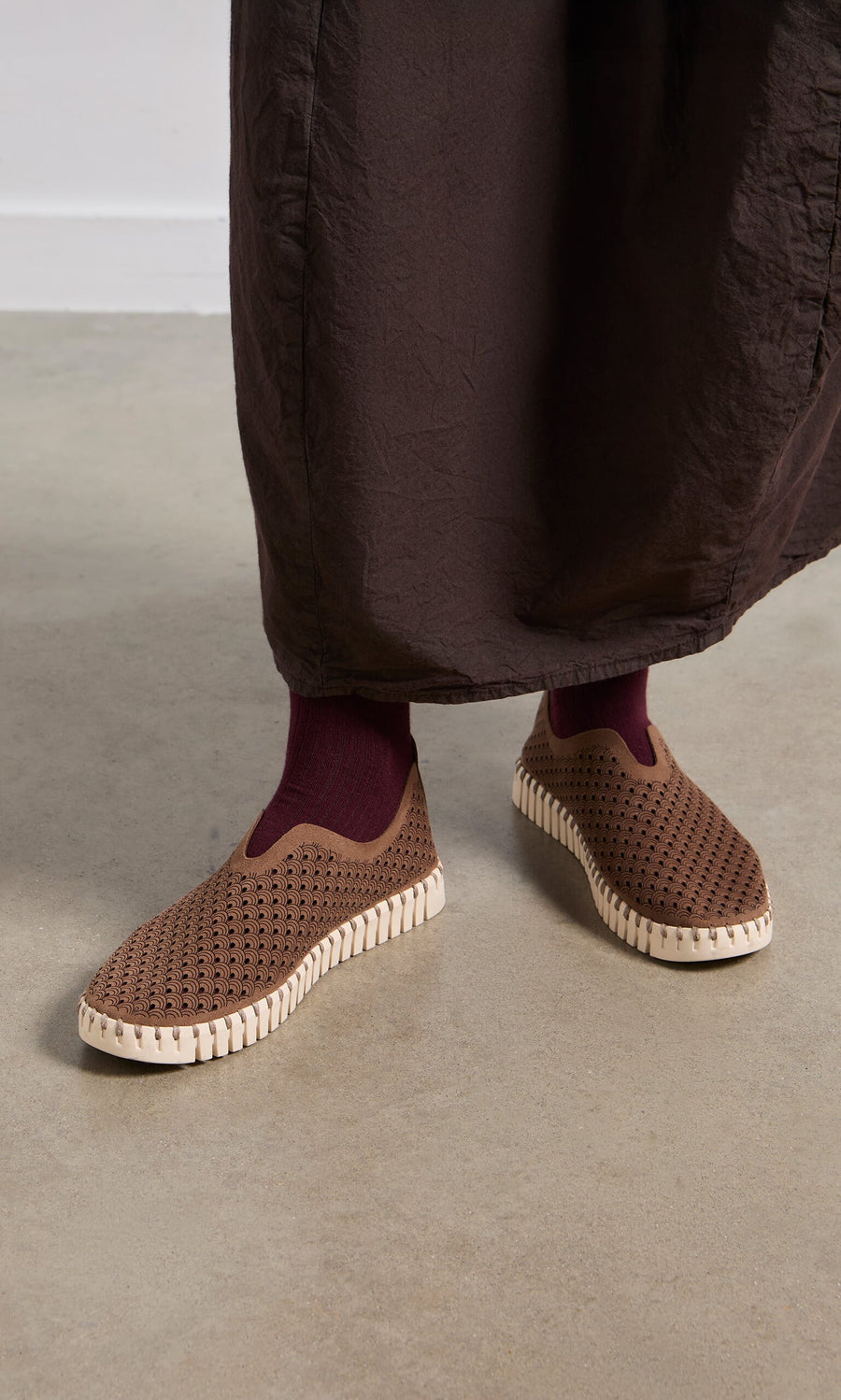Plümo- Person wearing Tulip Shoes - Brown with maroon socks and dark brown pants, standing on a light floor.