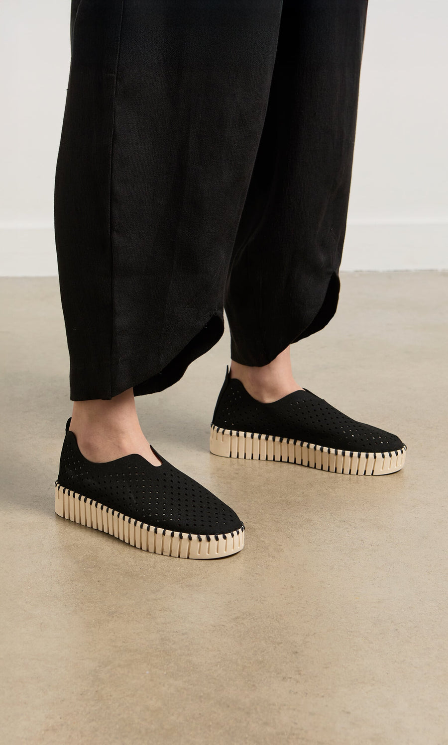 Plümo- Person wearing black wide-leg pants and Tulip Shoes - Carbon on a light brown floor.