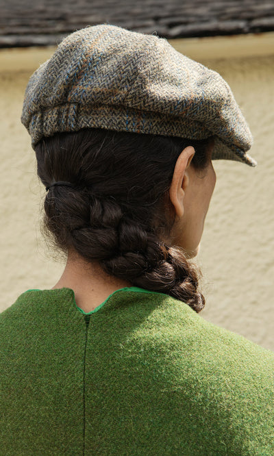 Plümo  Person with braided hair in a green top wears a Tweed Flat Cap, seen from behind against a light background.