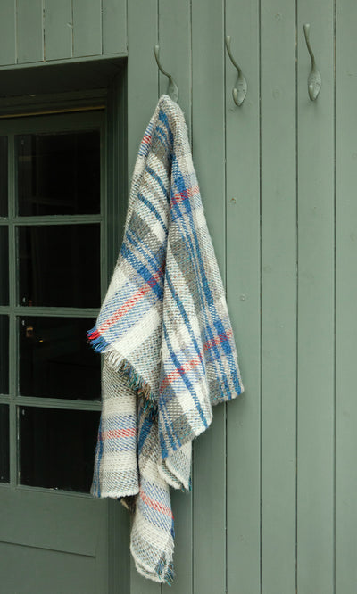 Plümo  A Random Throw in blue and red stripes hangs by a green wooden door.