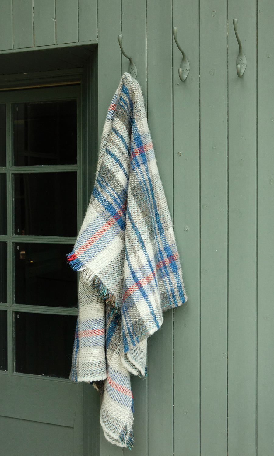 Plümo  A Random Throw in blue and red stripes hangs by a green wooden door.