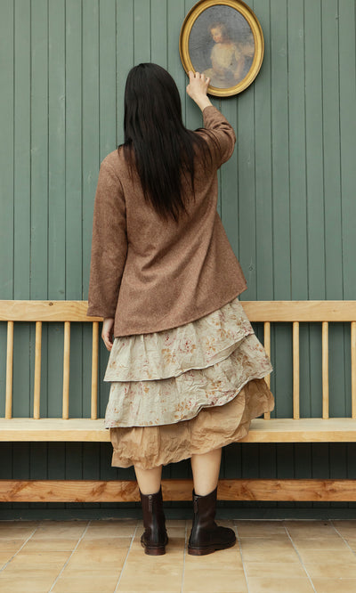 Plümo  Woman in the Tweedy Dress and a brown jacket stands on tiles, adjusting a portrait on the green wall.