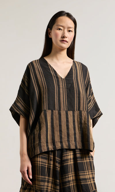 Plümo- Woman wearing the Westmorland Top with striped and checked panels, paired with a plaid skirt against a plain background.