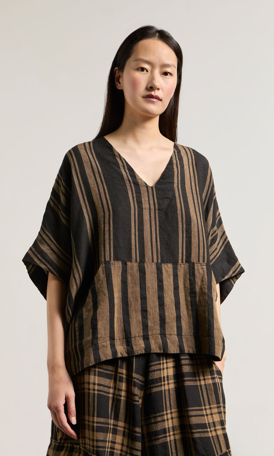Plümo- Woman wearing the Westmorland Top with striped and checked panels, paired with a plaid skirt against a plain background.