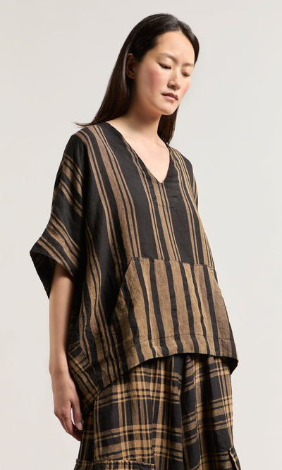 Plümo- Woman wearing the Westmorland Top—a loose woven linen V-neck with striped and checked panels, short sleeves, and a pocket.