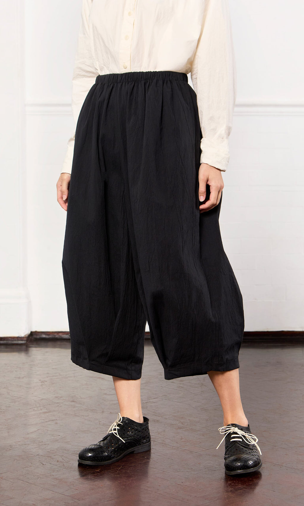 Plümo- Person wearing a white button-up shirt and Black Pinch Pants with lace-up shoes, standing indoors.