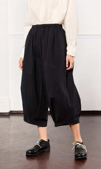Plümo- Person wearing a white button-up shirt and Black Pinch Pants with lace-up shoes, standing indoors.