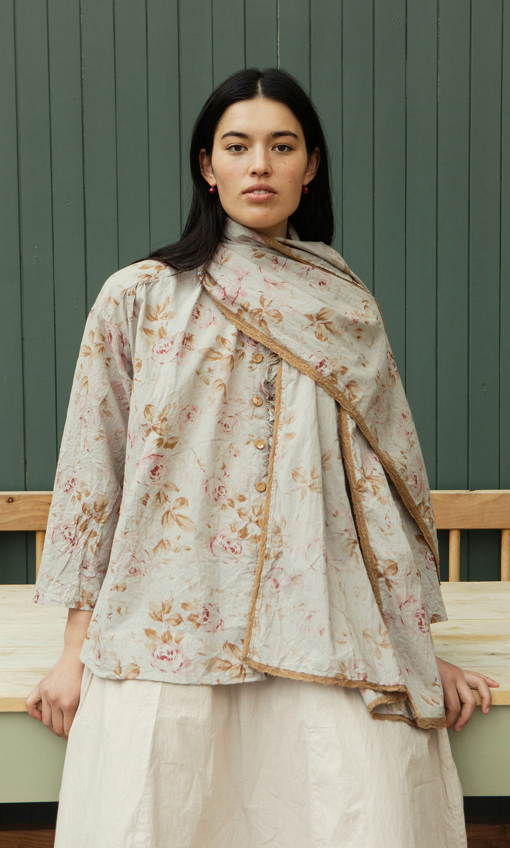 Plümo  Woman in a vintage floral top and the Dawn Scarf stands before green paneling, gazing at the camera.