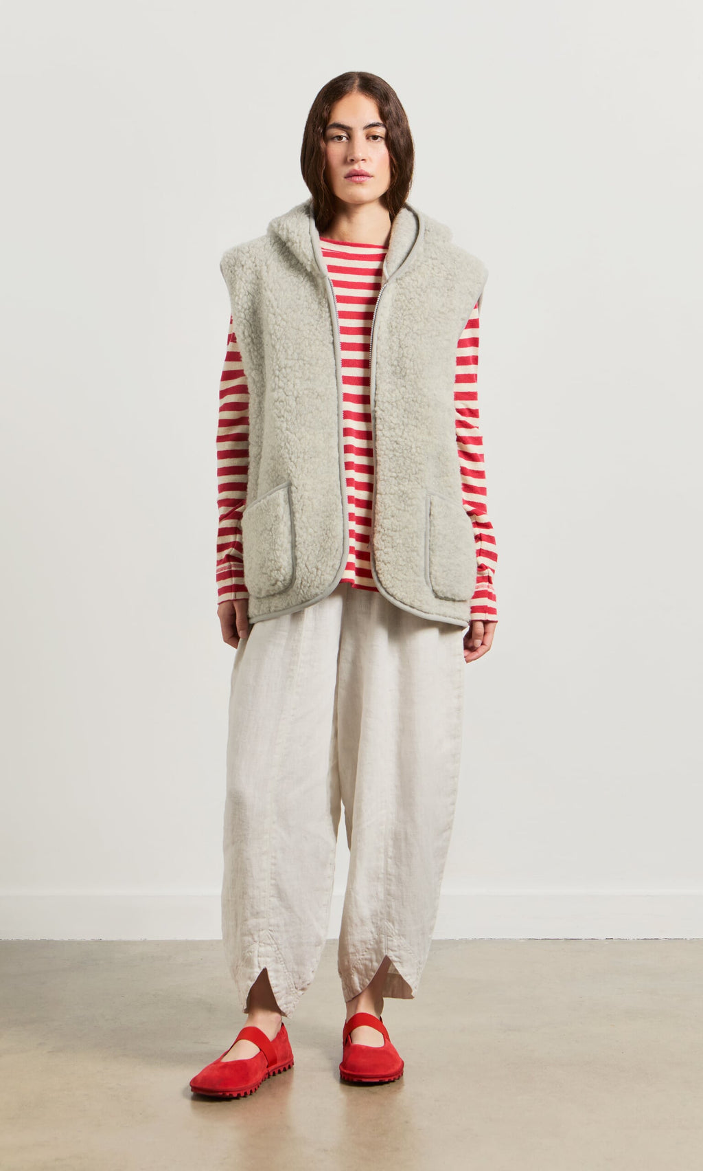 Plümo- Woman in a red-and-white striped top, Wool Gilet - Light Grey, loose white pants, and red shoes stands against a plain background.