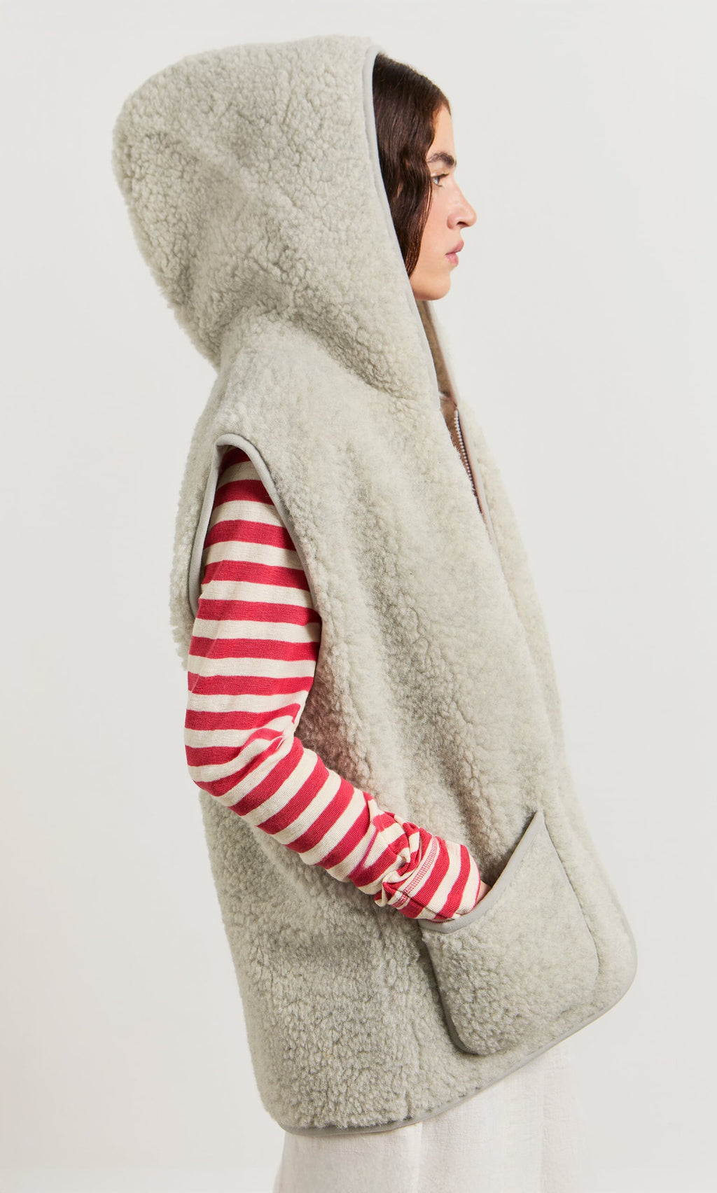 Plümo- Woman in a light grey Wool Gilet, styled as a vest, over a red and white striped long sleeve top, side profile.