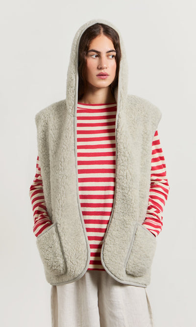 Plümo- Woman in a Wool Gilet - Light Grey over a red and white striped shirt, looking sideways.