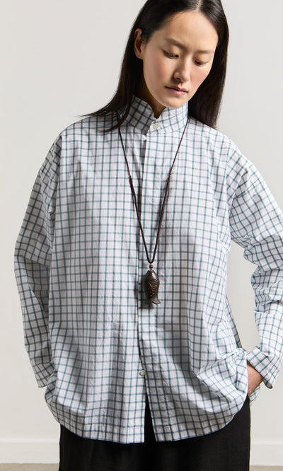 Plümo- Woman wearing the Yumi Fish Necklace with a loose checked shirt, looking down against a plain backdrop.