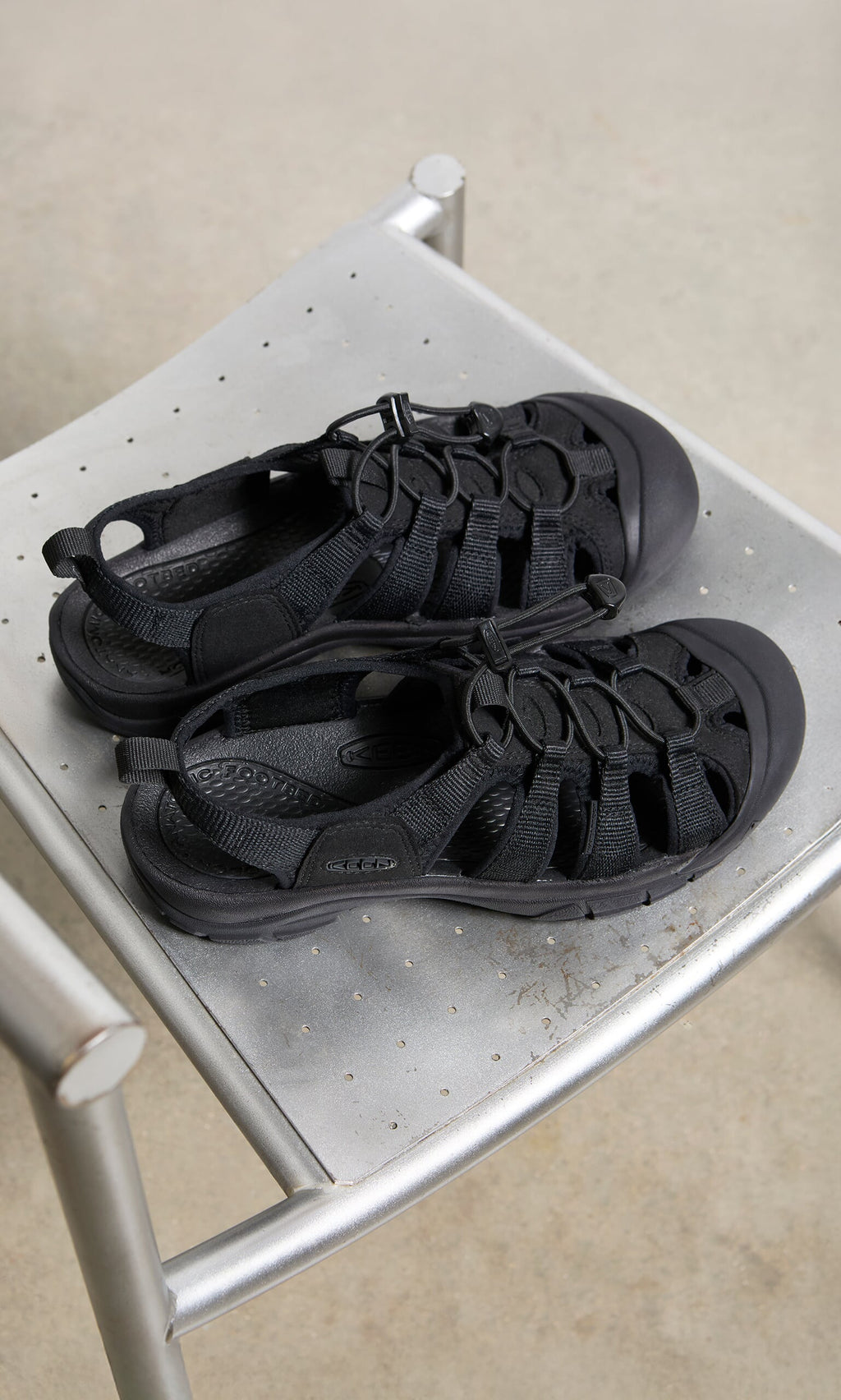 Plümo- A pair of black Newport Sandals with arch support on a metal chair with a perforated seat.