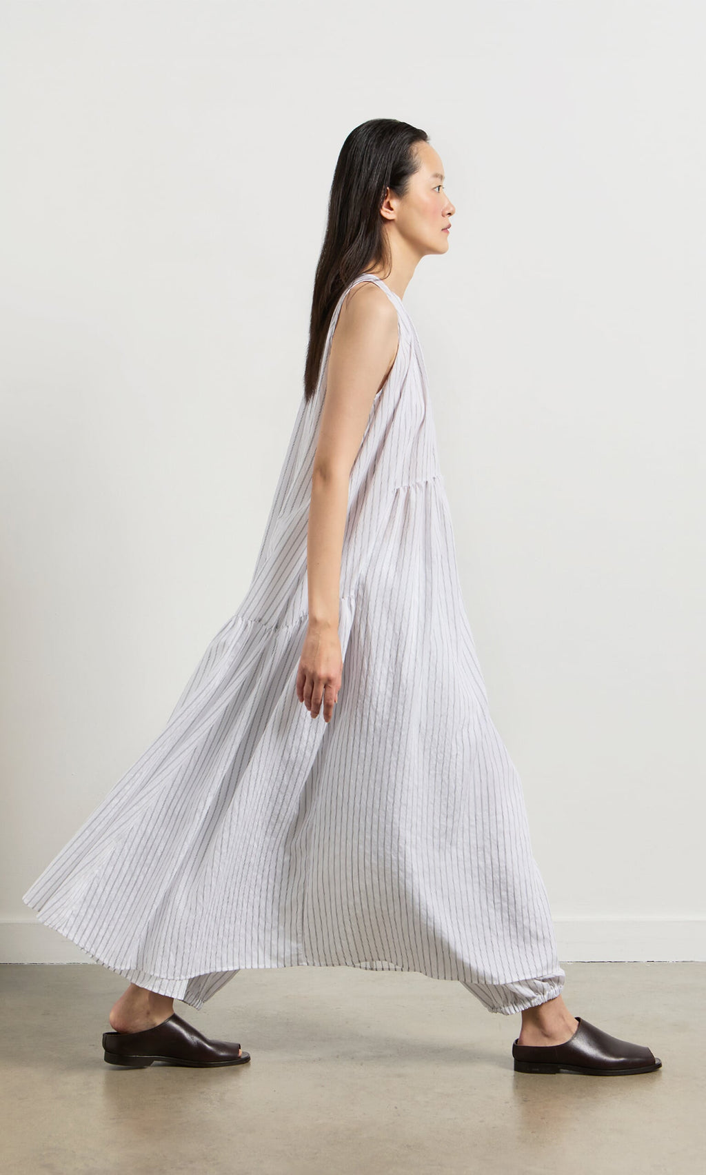 Plümo- A woman in the Alba Stripe Dress and black flats walks against a plain white background.