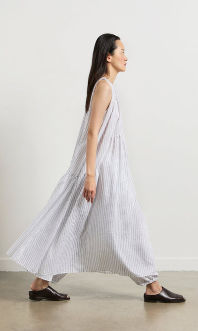 Plümo- A woman in the Alba Stripe Dress and black flats walks against a plain white background.
