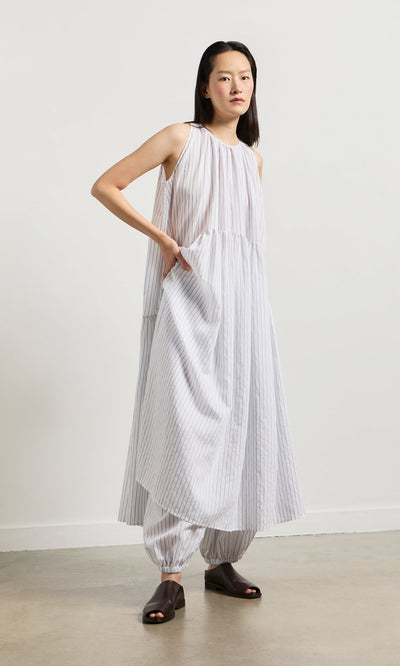 Plümo- Woman wearing the Alba Stripe Dress, a loose white pinstripe dress over matching pants, on a neutral background.