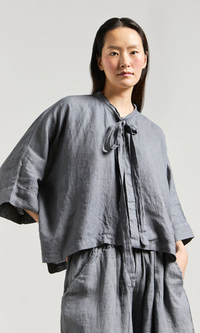 Plümo- A person wears the Antoine Blouse - Grey with a ribbon necktie and wide-leg pants against a plain background.