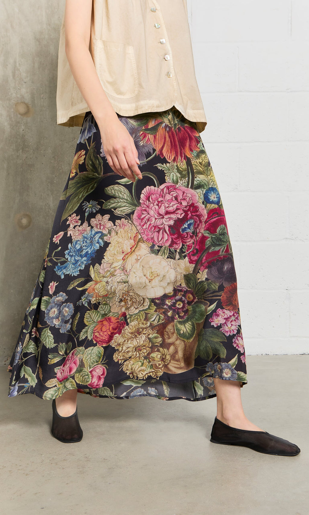 Plümo- Person wearing a beige top, Auricula Skirt, and black shoes on a concrete floor indoors.