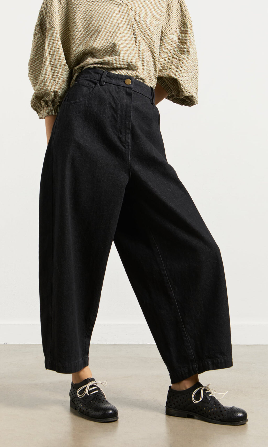 Plümo- Person wears a beige textured blouse, Black Barrel Pants, and lace-up shoes while standing on a light floor.