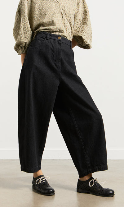 Plümo- Person wears a beige textured blouse, Black Barrel Pants, and lace-up shoes while standing on a light floor.