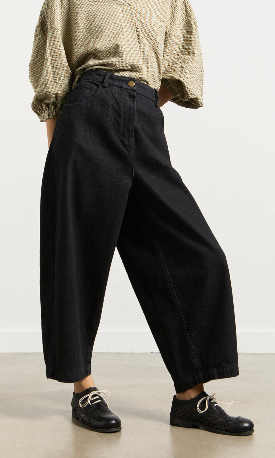 Plümo- Person wears a beige textured blouse, Black Barrel Pants, and lace-up shoes while standing on a light floor.