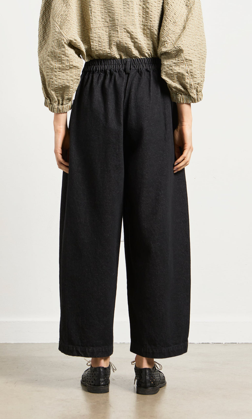 Plümo- Person stands on a light floor in relaxed silhouette, wearing Black Barrel Pants, black shoes, and beige long-sleeve top.