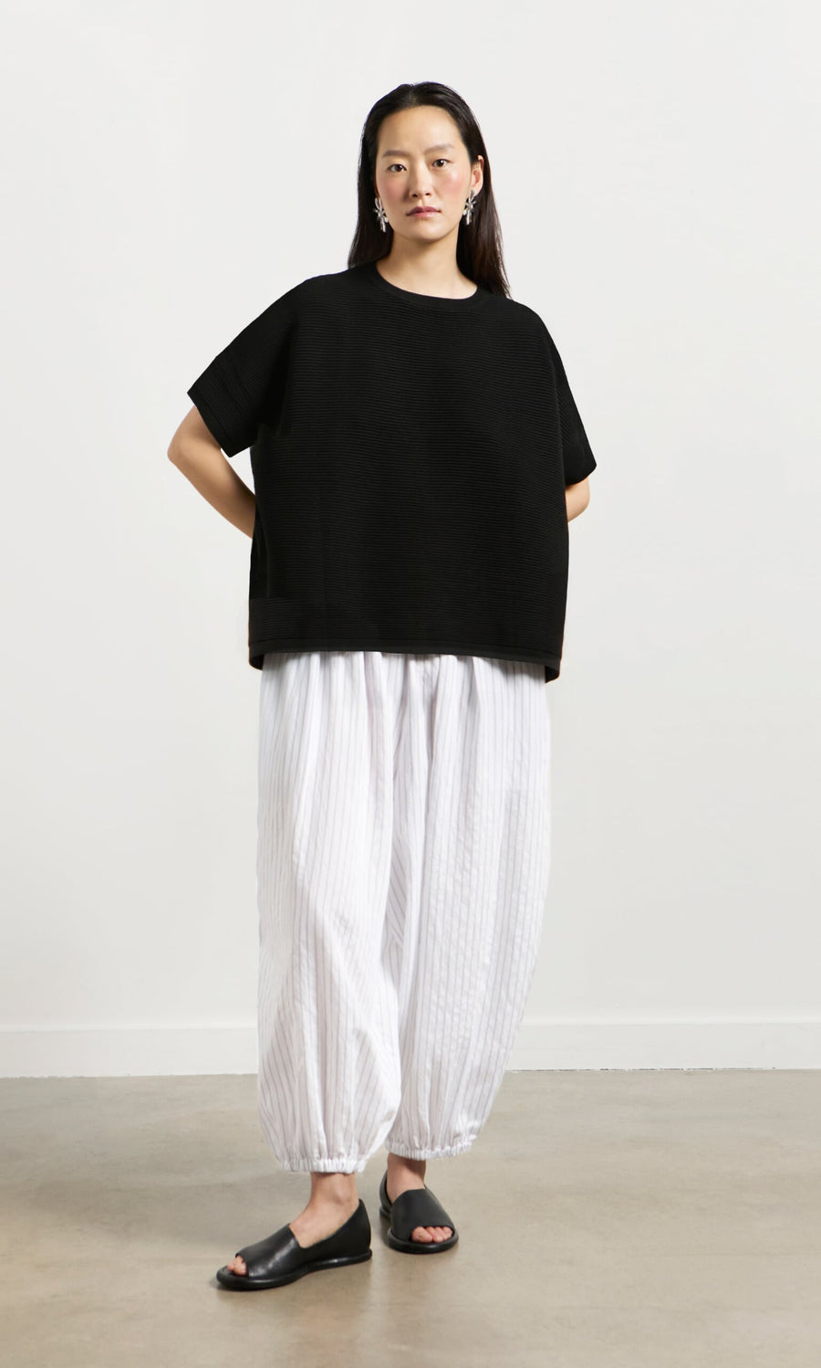 Plümo- Woman in Jack Short Sleeve - Black, white striped billowy pants, black sandals, on a plain background.