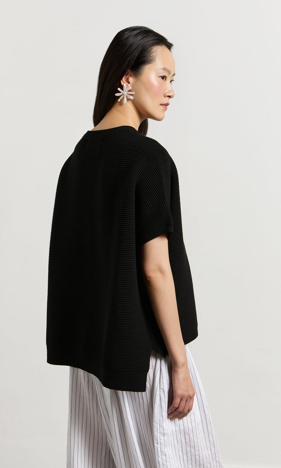 Plümo- Woman wears the Jack Short Sleeve - Black top with white striped pants and star earrings, standing against a plain background.