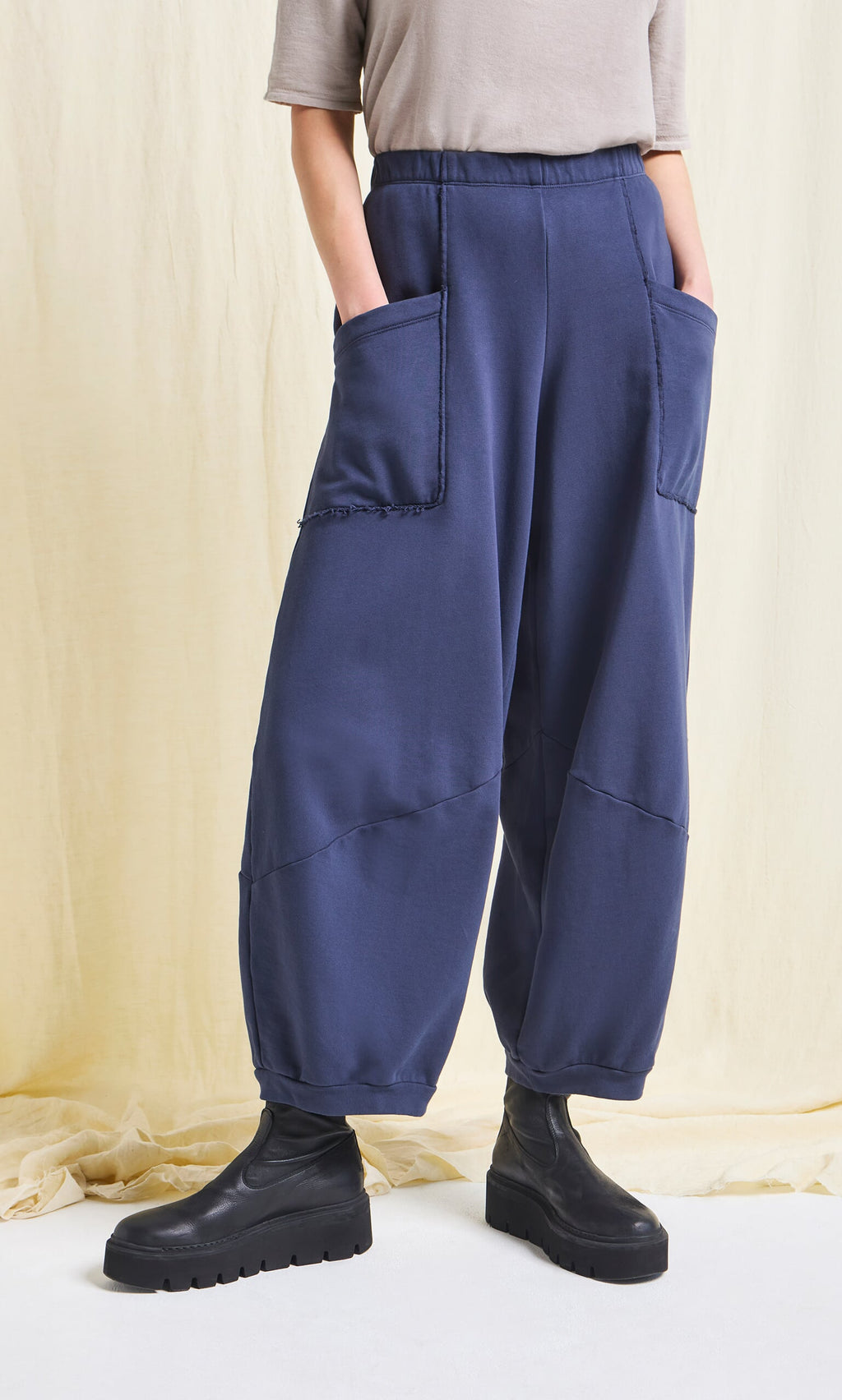 Plümo- Person wears Blue Barrel Pants with elastic waist, black boots, and a beige top against a light background.