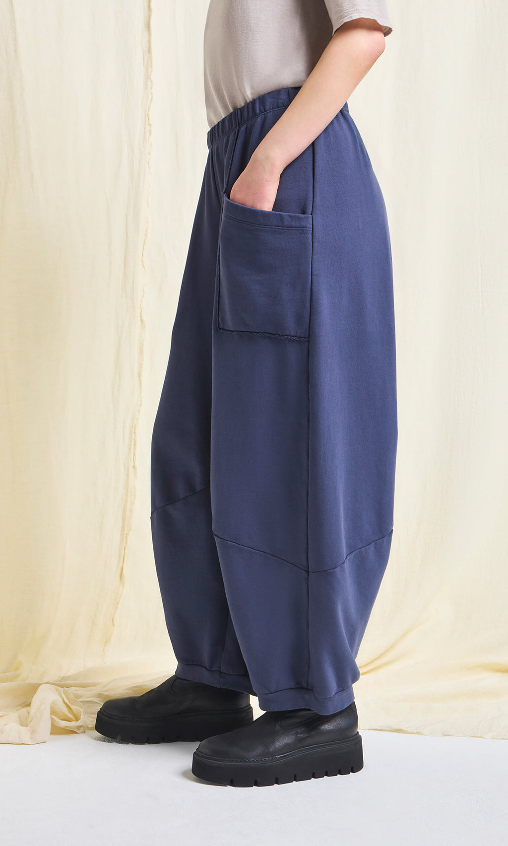 Plümo- Person in Blue Barrel Pants with elastic waist and raw edge details, styled with black platform shoes.