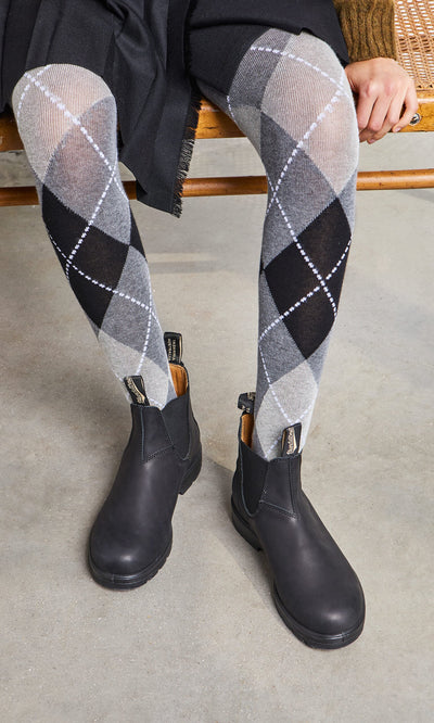 Plümo- Person wearing Blundstone Boots - Black and black, gray, and white argyle tights, sitting on a bench.
