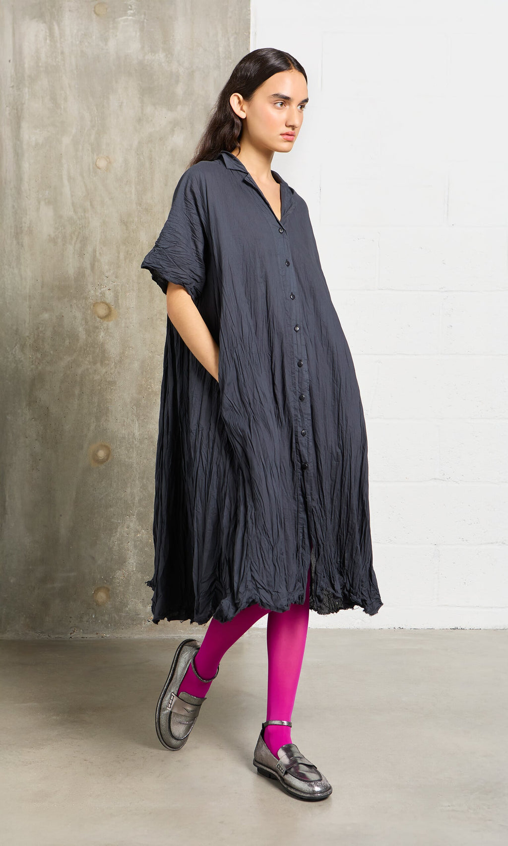 Plümo- A woman in a dark dress and Bright Magenta Tights stands in a modern, minimal space wearing silver shoes.