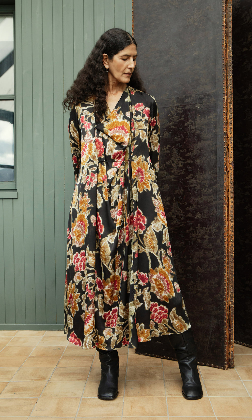 Plümo  Woman in the Brunn Dress and black boots stands on tile indoors, looking right. Plümo Studio style.