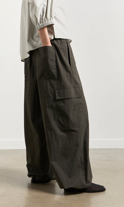 Plümo- Person wearing Cargo Pants with ankle bungees and a light long-sleeve shirt, standing indoors on a light floor.