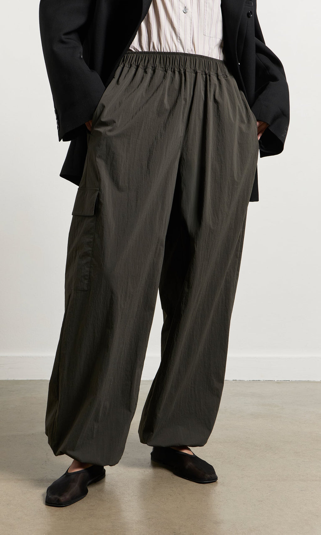 Plümo- Person wearing relaxed leg dark olive Cargo Pants, black blazer, and black shoes, standing on a light-colored floor.