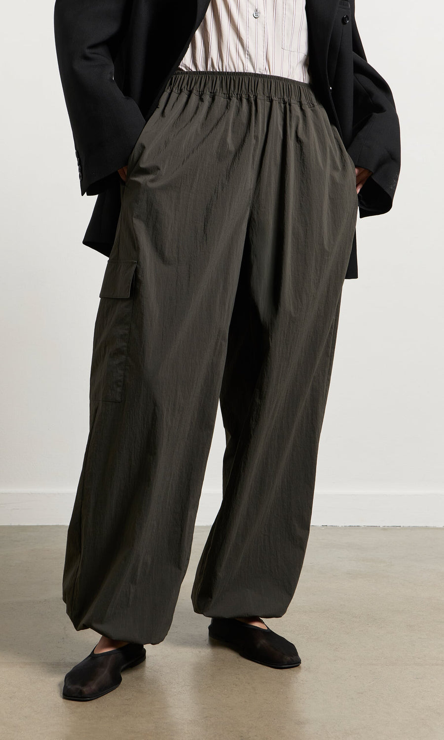 Plümo- Person wearing relaxed leg dark olive Cargo Pants, black blazer, and black shoes, standing on a light-colored floor.