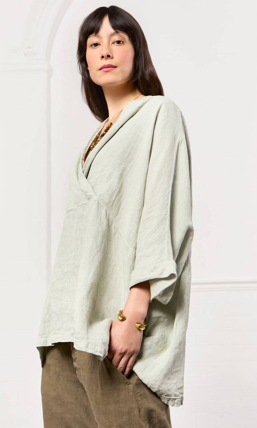 Plümo- Woman in Carvey Tunic with cropped sleeves and brown pants, standing confidently against a white background.