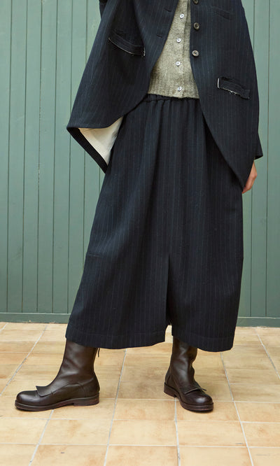 Plümo  Person wearing a Bo Skirt, black blazer, gray shirt, and dark brown boots while standing indoors.