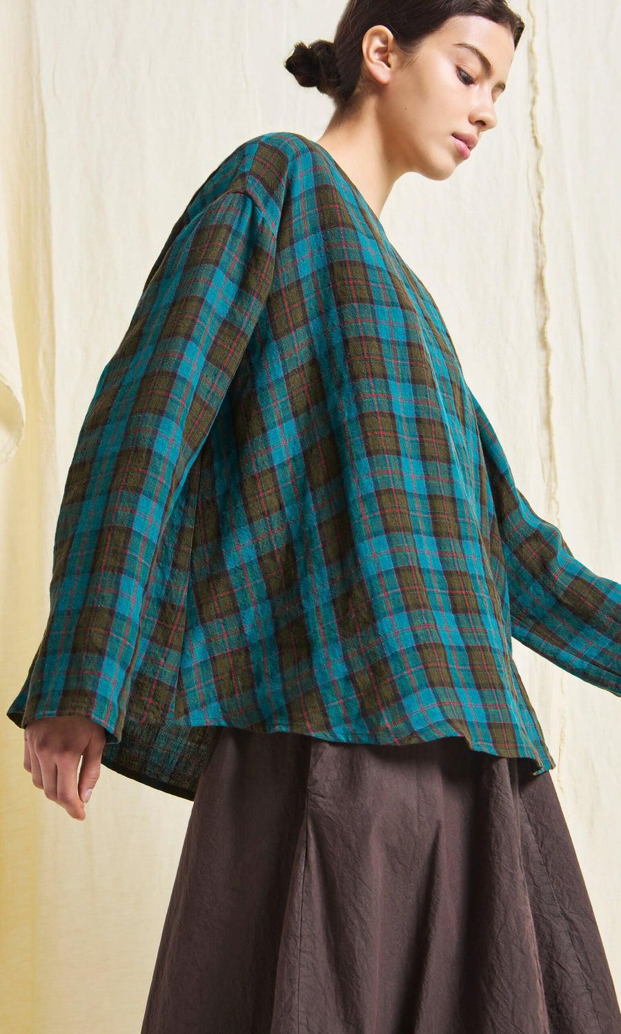 Plümo- Woman in a loose Clodagh Blouse, blue and green tartan with wide sleeves, paired with a brown skirt.