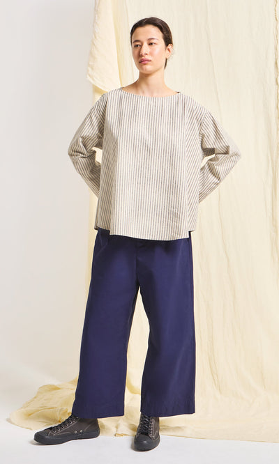 Plümo- Person wears a beige striped top, Cromer Pants - Navy, and black shoes, standing before a cream fabric backdrop.